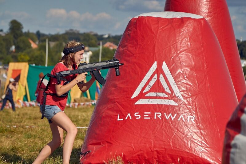 Девочка в красной футболке с бластером LASERWAR у укрытия.