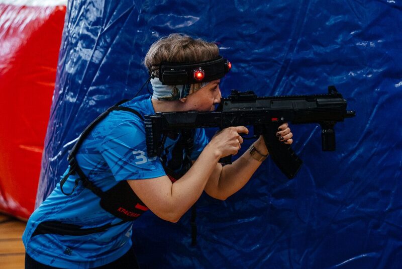 Девушка в синей форме LASERWAR прицеливается из оружия.
