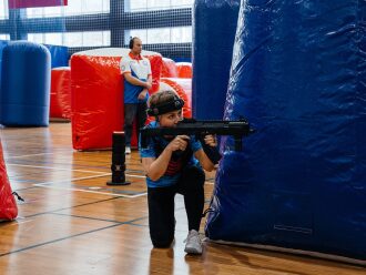 Игрок LASERWAR в синей форме прицеливается из укрытия.