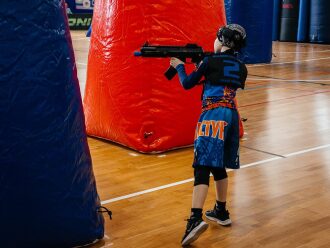 Юный боец LASERWAR в синей форме целится из укрытия.