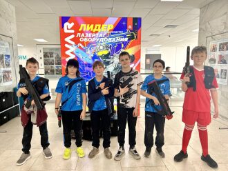 Группа юных бойцов LASERWAR с оружием позирует перед баннером.