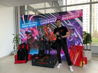 Молодой человек демонстрирует лазертаг-автомат у баннера LASERWAR.