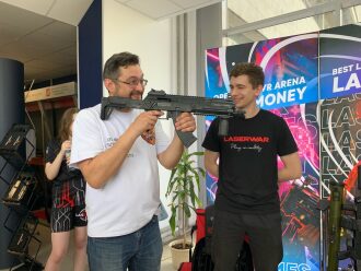Мужчина демонстрирует лазертаг-оружие молодому человеку.