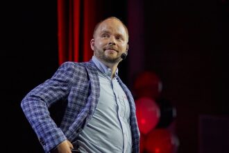 Мужчина в пиджаке с микрофоном на сцене.