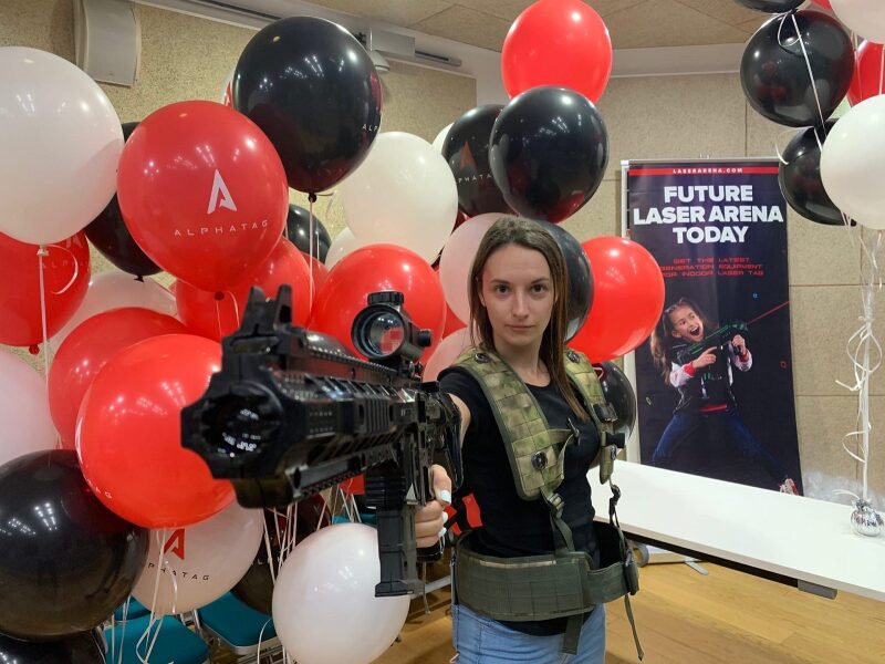 Девушка в тактическом жилете с лазертаг-винтовкой.