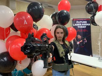 Девушка в тактическом жилете с лазертаг-винтовкой.
