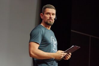 Мужчина с микрофоном держит папку с документами.