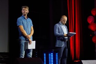 Два спикера на сцене с документами.