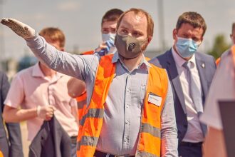 Мужчина в маске и жилете указывает направление.