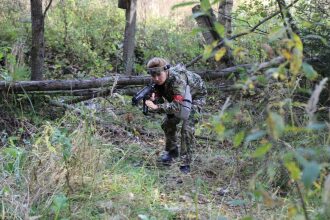 Боец LASERWAR в камуфляже пригнулся у поваленного дерева