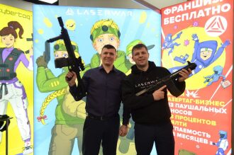 Два мужчины демонстрируют оружие LASERWAR на выставке.