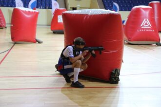Мальчик LASERWAR прицеливается из-за красного укрытия.