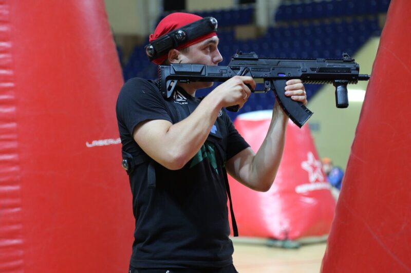 Игрок LASERWAR с оружием занимает позицию у красного укрытия.