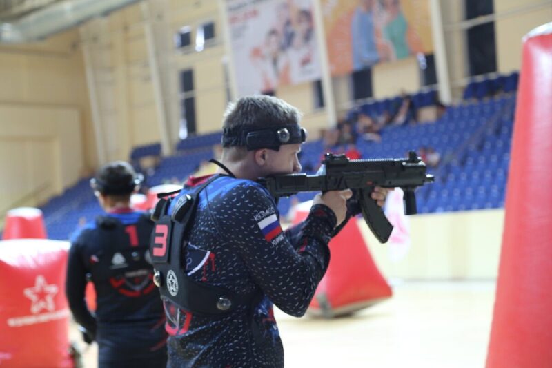 Боец LASERWAR с оружием на арене с красными укрытиями.
