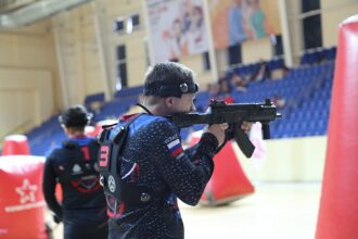 Боец LASERWAR с оружием на арене с красными укрытиями.