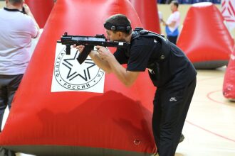 Боец LASERWAR прицеливается из-за красного укрытия с логотипом.
