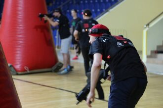 Игрок LASERWAR в движении с оружием у красного препятствия.