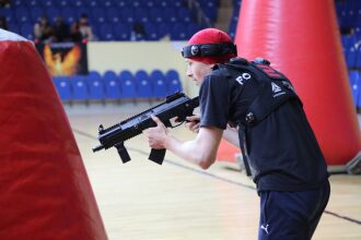Игрок LASERWAR прицеливается из-за красного надувного укрытия.