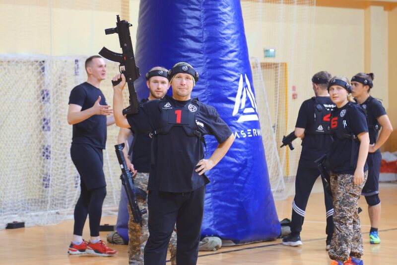 Боец LASERWAR демонстрирует оружие перед синим укрытием.