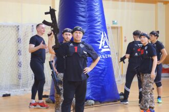Боец LASERWAR демонстрирует оружие перед синим укрытием.
