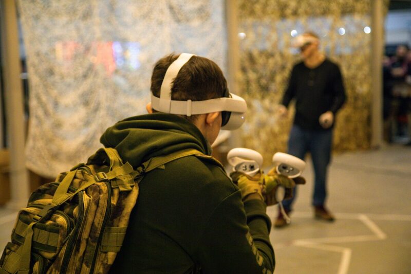 Игрок в VR-гарнитуре LASERWAR с контроллерами готовится к виртуальному сражению.