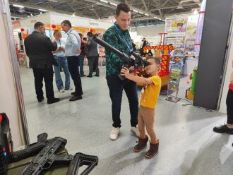 Мальчик целится из лазертаг-винтовки под присмотром взрослого.
