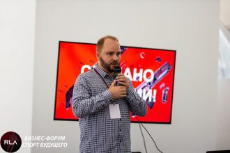 Спикер LASERWAR с микрофоном на фоне экрана
