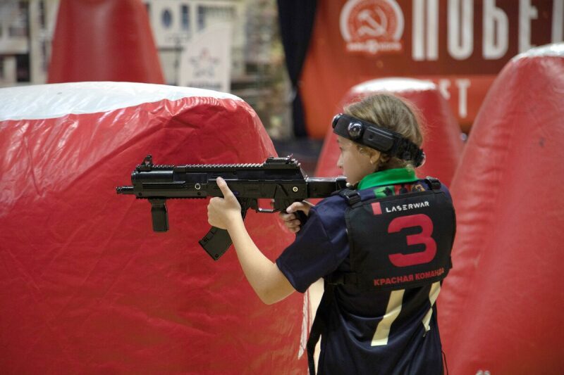 Девочка в жилете LASERWAR целится из оружия