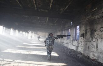 Боец LASERWAR в камуфляже ведет огонь в заброшенном здании.