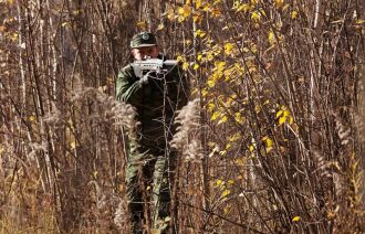 Осенний лес: боец LASERWAR в камуфляже целится.