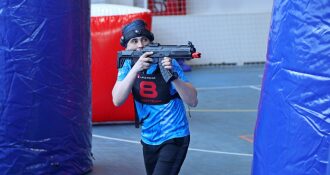 Игрок в синей форме с автоматом LASERWAR укрывается за надувной конструкцией.
