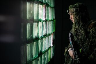Игрок в маскировочном костюме у стены из стеклянных блоков