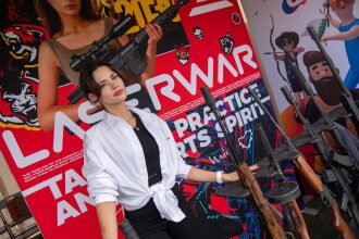 Модель позирует с лазертаг-оружием на фоне стенда LASERWAR.