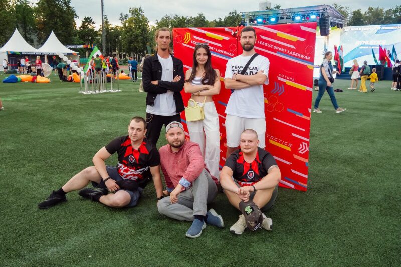 Группа товарищей позирует на фоне яркого баннера LASERWAR.