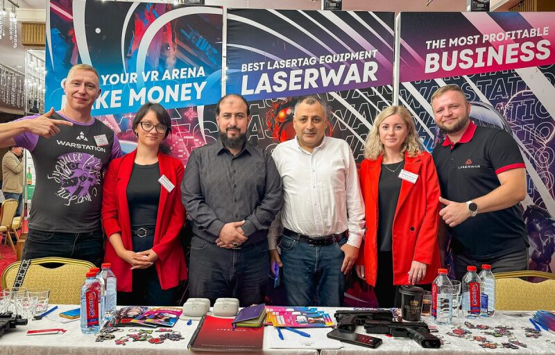 Команда LASERWAR позирует на фоне баннеров.