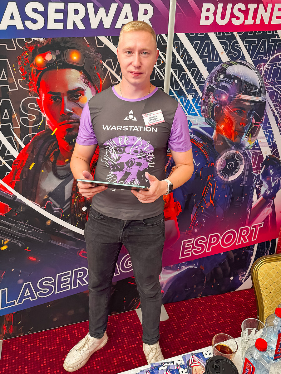 Мужчина держит планшет на фоне футуристичных баннеров LASERWAR.
