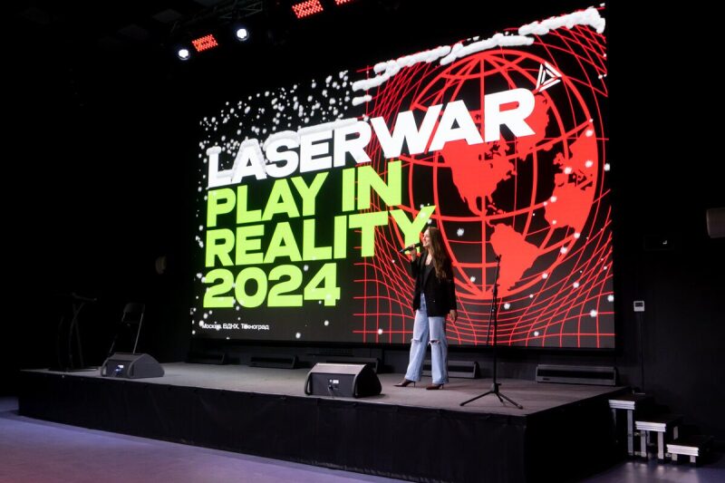 Девушка с микрофоном на сцене перед экраном LASERWAR