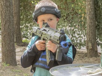 Мальчик LASERWAR прицеливается из-за дерева.