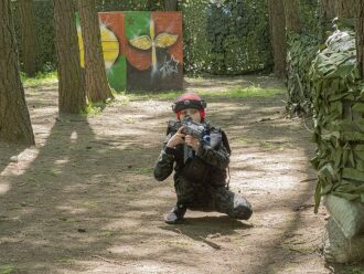Юный боец LASERWAR в камуфляже прицеливается из-за дерева.