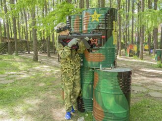 Юный боец LASERWAR целится из-за камуфляжных бочек.