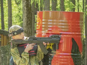Юный боец LASERWAR прицеливается из-за бочек.