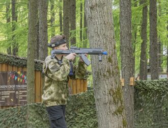 Юный стрелок LASERWAR прицеливается из-за ствола дерева.