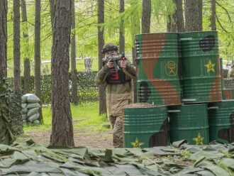 Юный боец LASERWAR прицеливается из-за камуфлированных бочек.