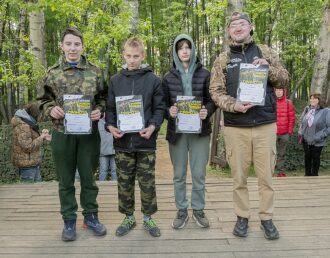 Победители турнира LASERWAR с грамотами позируют на деревянной сцене.