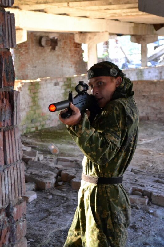 LASERWAR: сосредоточенный боец в камуфляже целится из укрытия.