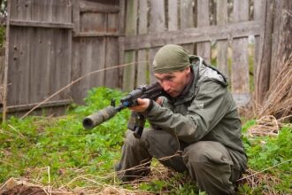 Боец LASERWAR в прицеле, затаившись у деревянного забора.