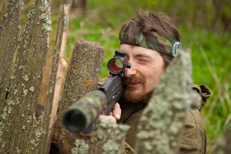 Боец LASERWAR с прицелом высматривает противника из-за забора.