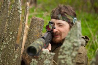 Боец LASERWAR с прицелом высматривает противника из-за забора.