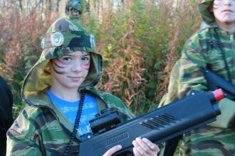 Мальчик с раскрашенным лицом держит лазертаг-винтовку