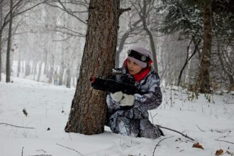 Девочка в засаде с лазертаг-винтовкой в зимнем лесу